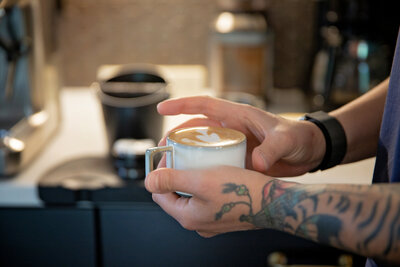 tattooed hand holding coffee during video consulting in Denver, CO at Pixel Lustre