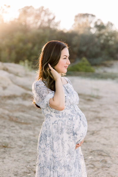 expecting mother standing holding her baby bump touching her hair taken by Sacramento Maternity Photographer Kelsey Krall Photography