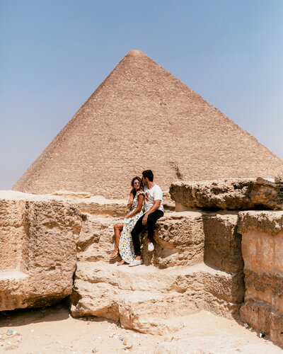 man and woman sitting in front of egyptian pyramid