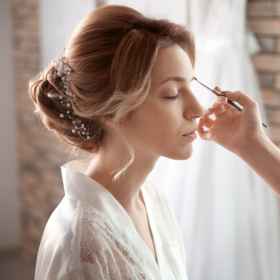 Bride getting her makeup done on her wedding day wearing a white lace robe
