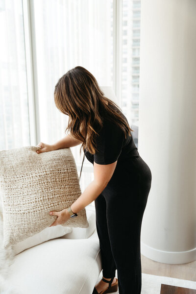 Online interior decorator, Michelle, wearing a black jumpsuit and fluffing a throw pillow