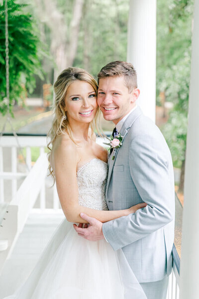 a blonde bride in her wedding gown hugs her groom in his suit close for a portrait on a porch
