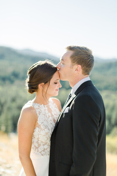 groom kissing brides forehead with mountains in the background