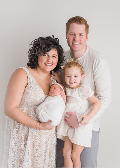 a family with their newborn  and all white clothes and a white background