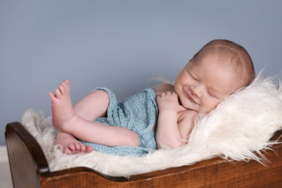 Beautiful Mississippi Newborn Photography: sleeping newborn boy smiling while wrapped in blue in a wooden cradle