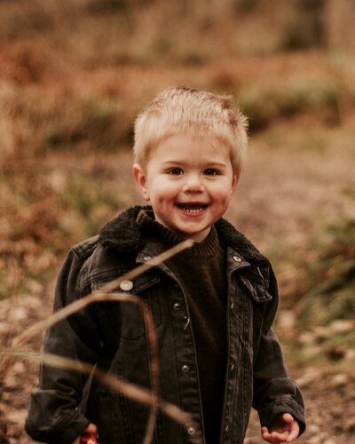 Young boy grinning at the camera in a woodland setting