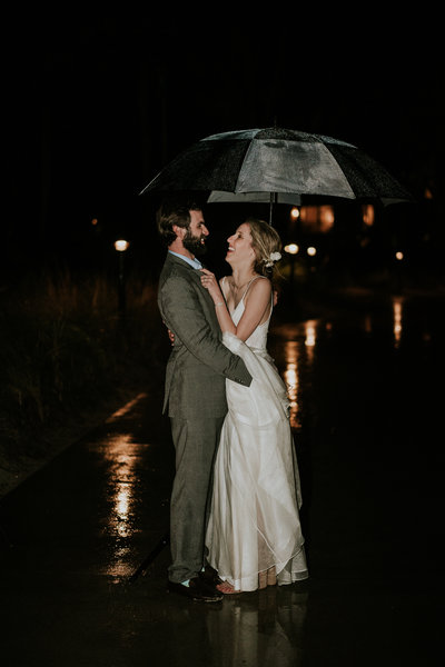 Wedding couple embraces under an umbrella in the rain at night at Sandpiper Bay Club Med