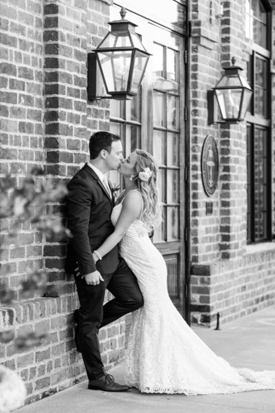 black and white of bride and groom kissing against brick