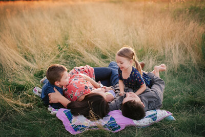 family with young children laying down snuggling in field on blanket in rosemount