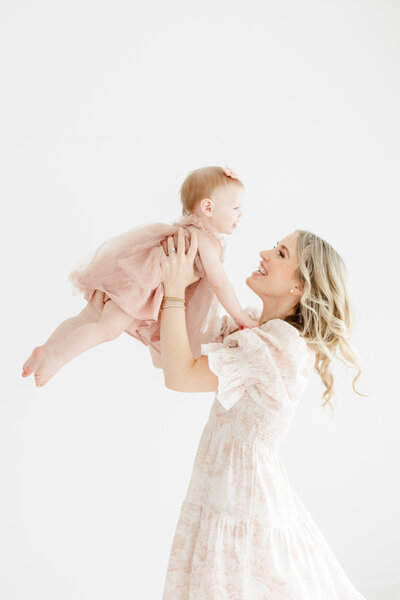 Mother in flowing dress spins her baby girl in the air during baby milestone portrait session