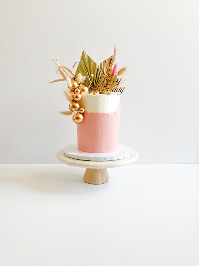 Pink and white birthday cake topped with gold decorations and a happy birthday sign.