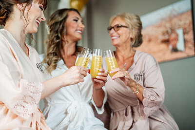 bride and bridesmaids clinking mimosa glasses while getting ready