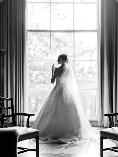Black and white portrait of a bride by a large window in Larz Anderson House in D.C.