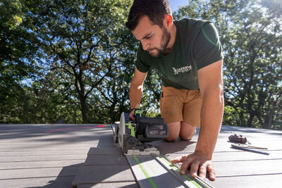 Josh Ferri, owner of Lakeside Decking, using a track saw to cut deck boards on a summer day. 