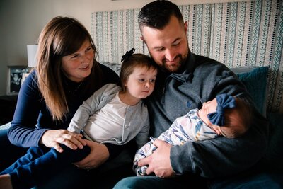 Family of four cuddled on bed looking at newborn. Lifestyle family session by Jennifer Beal Photography.