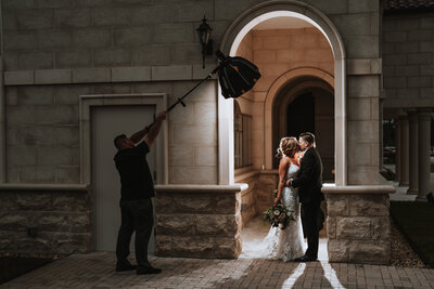 bride and groom kissing while photographer holds light above them