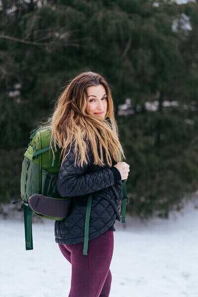 Gina wearing a green backpack, looking over her shoulder with a slight smile