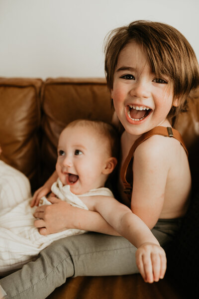 toddler and baby brother laughing on the couch