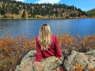 Colorado elopement photographer sitting on rocky overlook by a mountain lake in fall, scouting locations for adventurous elopement photos