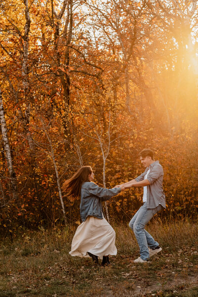 Couple twirling in the fall leaves and golden hour light