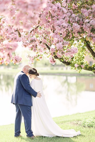 a bride and groom hugging under a tree with pink blossoms