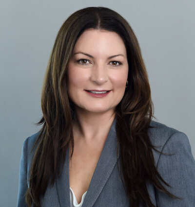 Corporate female headshot with brown hair and grey suit jacket