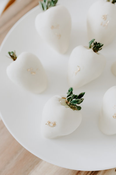 White chocolate dipped strawberries with gold leaf accents on a white plate.