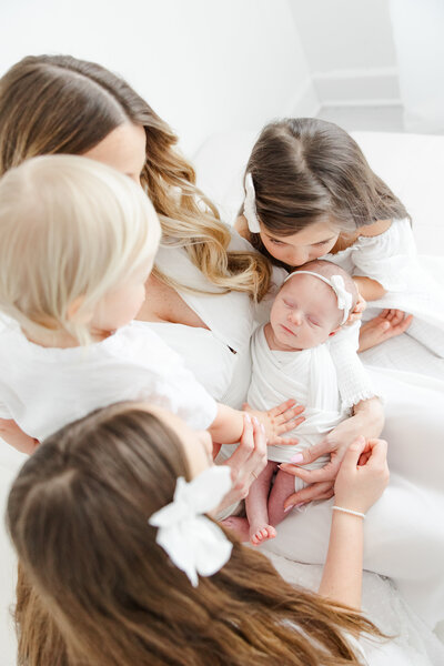 Mother holds sleeping newborn baby girl as her 3 older children look on during newborn portrait session
