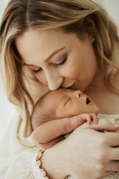 Sydney mother kissing her sweet newborn boy who has his eyes closed and mouth opened sleeping.