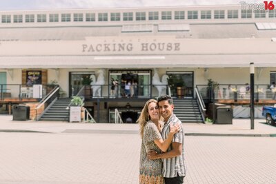 Engaged couple cuddle up as they pose for engagement photos in front of the Anaheim Packing House