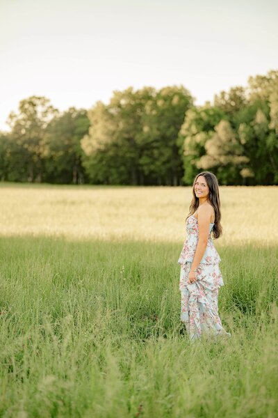 charlotte graduate wearing a flower deress standing in a tall grassy field