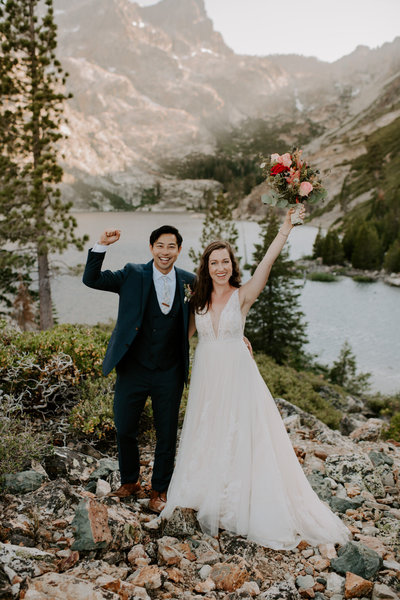 bride and groom with hands in the air while smiling with mountains in background