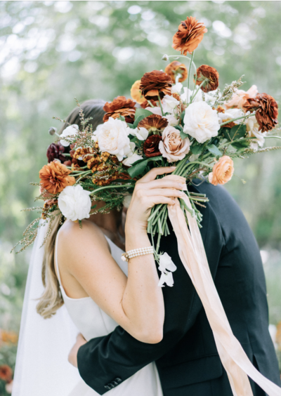 bride and groom kiss behind bouquet