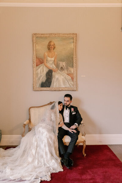 Couple sitting together on wedding day in front of painting at Rosecliff Mansion in Newport, RI