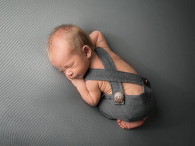 Studio newborn session of baby boy wearing gray overalls.
