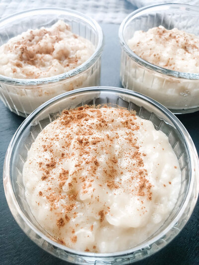 three servings of rice pudding in glass jars with cinnamon powder.