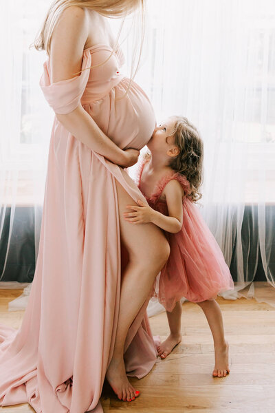 Portland mom in pink dress in  Portland Studio. her daughter is kissing her belly.