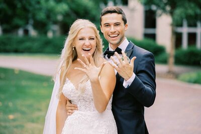 Bride and groom smiling holding up wedding rings