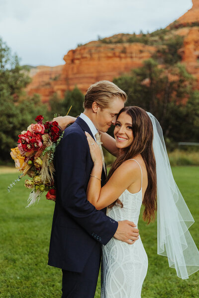 bride smiling at teh camera as her groom holds her in sedona landscape