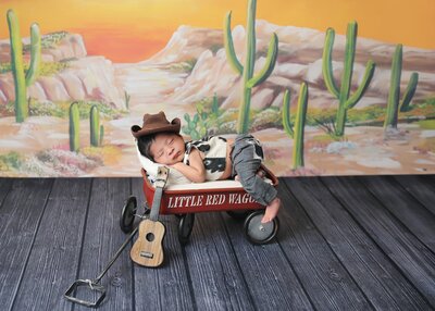 Sleeping newborn cowboy in little red wagon.