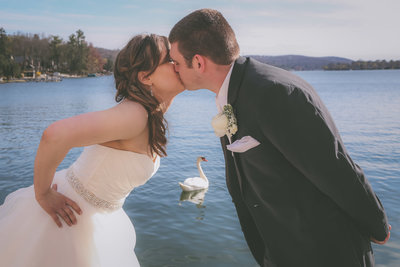 A couple kisses among a lake with a swan spying on them.