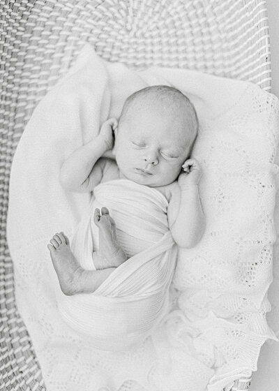 A black and white portrait of a newborn baby laying in a basket on a knitted blanket that was taken in a photography studios in Dallas.