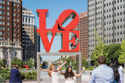 Two brides holding hands outdoors at Love Park in Philadelphia.