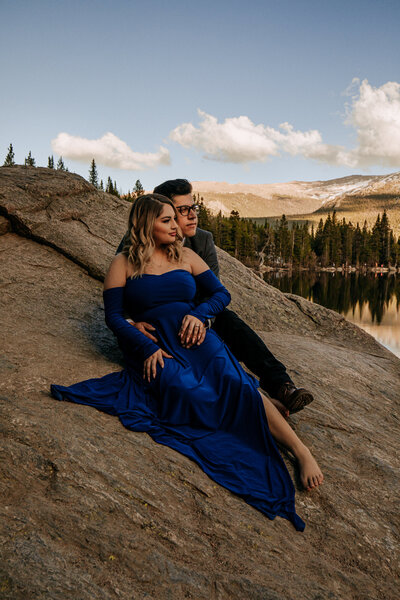Engaged couple sits and hold each other while sitting on rock on Bear Lake