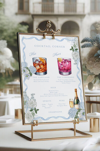 Signature drink sign displayed in an elegant gold frame atop a rustic wooden bar, styled for a French blue summer wedding in Jackson, WY.