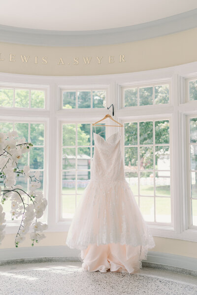Beautiful wedding dress hung in window with soft light coming through, captured by NY wedding photographer, Mary Fosky