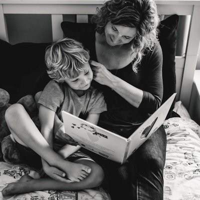 At home lifestyle portrait of mom reading to son on bed. Photo in black and white.