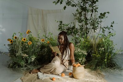 Black woman on the ground surrounded by foliage reading a book
