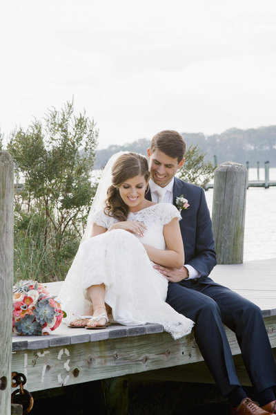 bride and groom sit on dock at clarks landing yacht club wedding