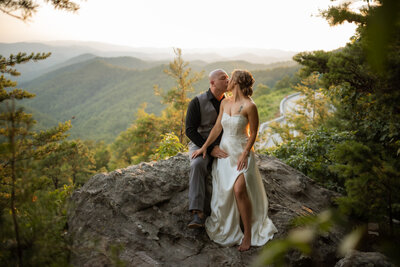 couple eloping to Gatlinburg in the Foothills as they sit on a rock together in the woods with the Smoky Mountains in the distance 